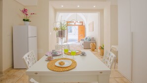 A dining area with a white table set for two, a white refrigerator, and a potted plant on the left.