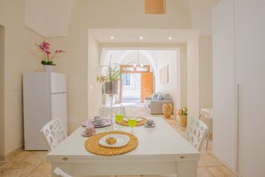 Een eethoek met een witte tafel gedekt voor twee personen, een witte koelkast, en een potplant aan de linkerkant.