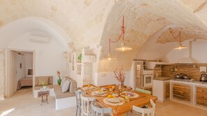 Cozinha ampla com mesa de jantar de madeira, cadeiras brancas e teto de pedra.
