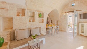 Quarto com paredes de pedra, um sofá, uma mesa de jantar com cadeiras e uma área de cozinha com armários.