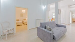 Un soggiorno moderno con un divano grigio, una poltrona bianca e un letto nella stanza adiacente.