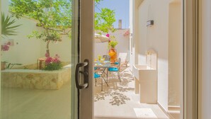 Porta aperta su un patio luminoso con tavolo, sedie e un vaso di fiori.