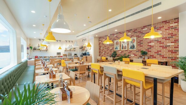 Un restaurante moderno con varias zonas de comedor, incluyendo una mesa común alargada y cabinas individuales.