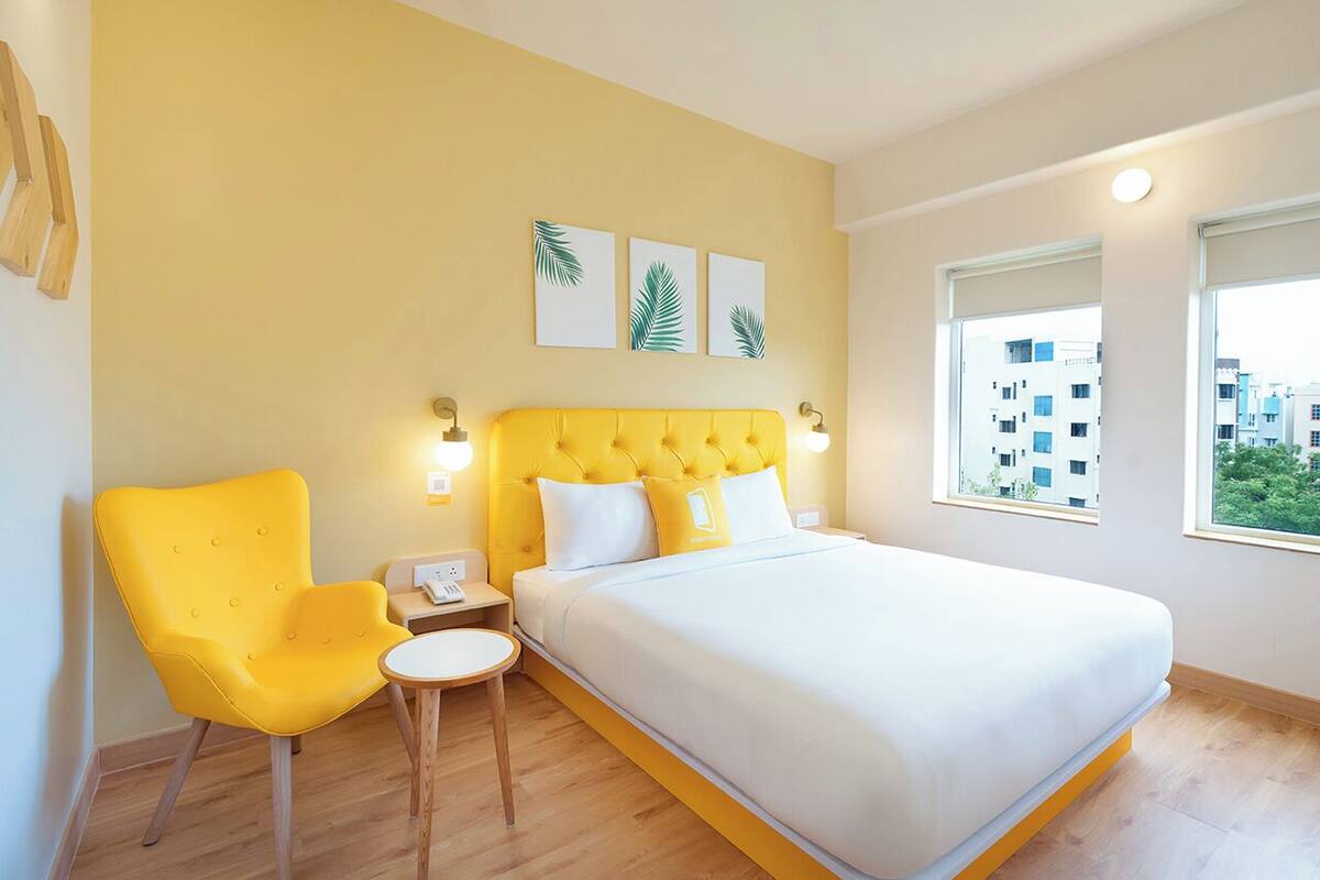 A bedroom with a yellow upholstered chair, a bed with white bedding, and a small round table.