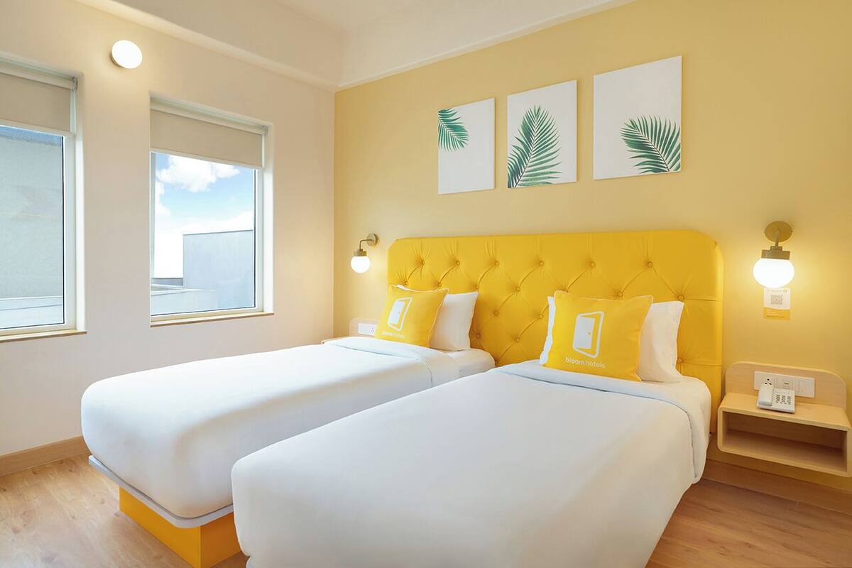 A hotel room with two beds, a yellow headboard, and a view of the city.