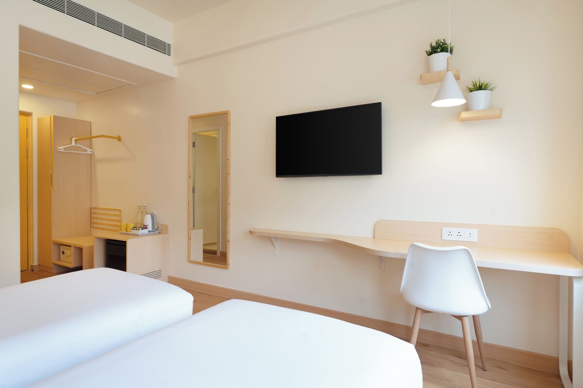 Habitación de hotel con cama, escritorio, silla, televisor y espejo.