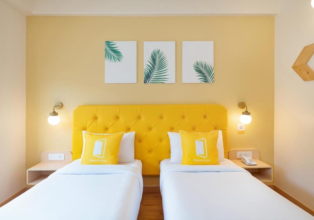 Een hotelkamer met twee bedden, een geel hoofdeinde en drie kunstwerken van palmbladeren aan de muur.