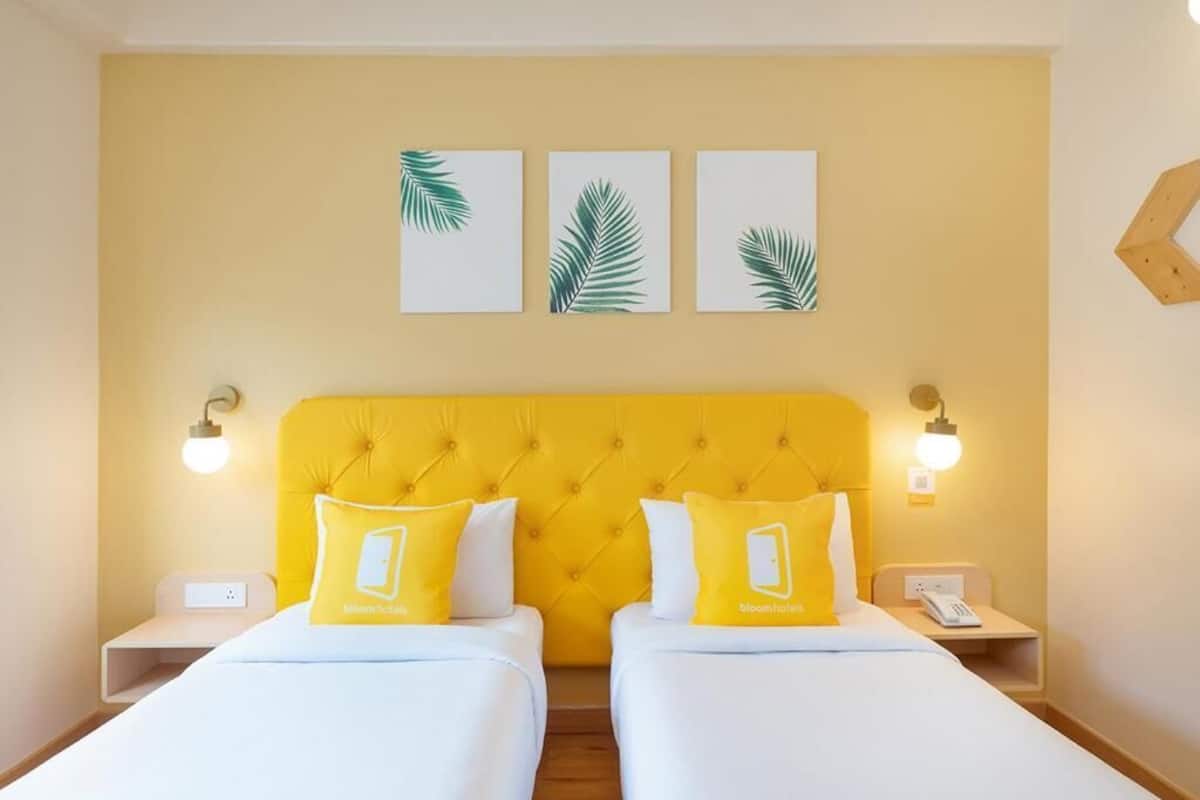A hotel room with two beds, a yellow headboard, and three palm leaf wall art pieces.