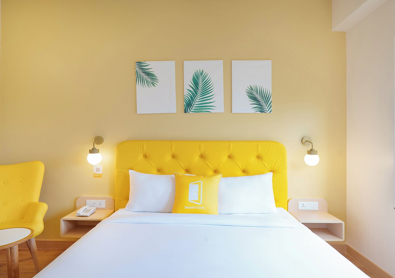Une chambre d’hôtel avec une tête de lit jaune, du linge de lit blanc et un lit avec deux oreillers. Il y a deux tables de chevet, chacune avec une lampe, et un téléphone sur l’une d’elles.