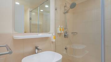 A modern bathroom with a white sink, a glass shower enclosure, and a mirror above the sink.