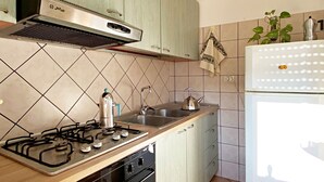 Μια κουζίνα με ανοιχτόχρωμα πράσινα ντουλάπια, μια κουζίνα αερίου, ένα βραστήρα, έναν νεροχύτη και ένα λευκό ψυγείο.