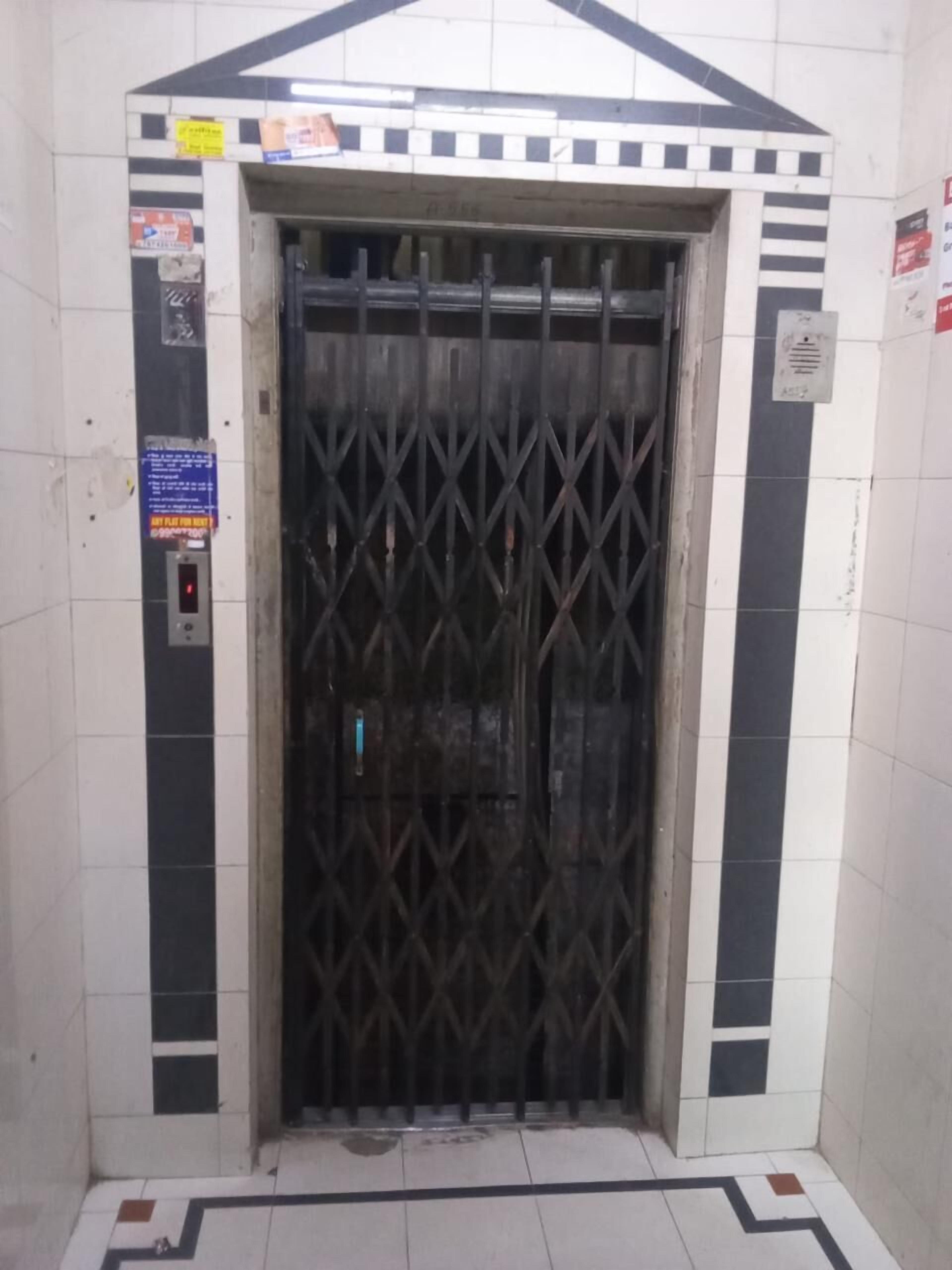 Un ascensor con puerta de rejilla metálica, rodeado de paredes con baldosas de diseño geométrico.