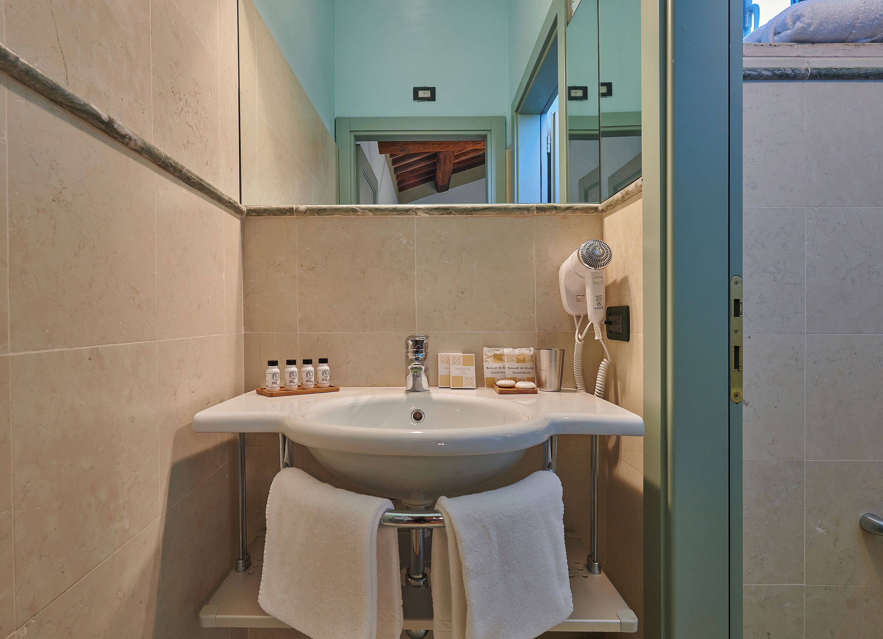 A bathroom with a sink, mirror, hairdryer, and toiletries.