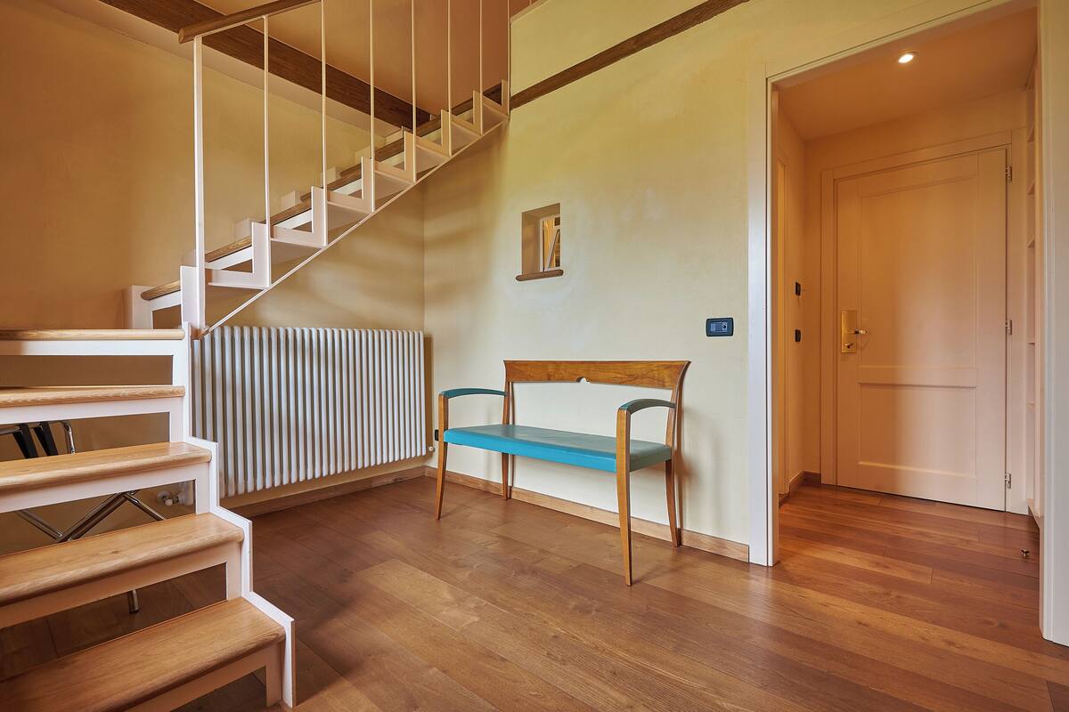 Un escalier avec des marches en bois et des rampes blanches, un banc en bois et un radiateur fixé au mur.