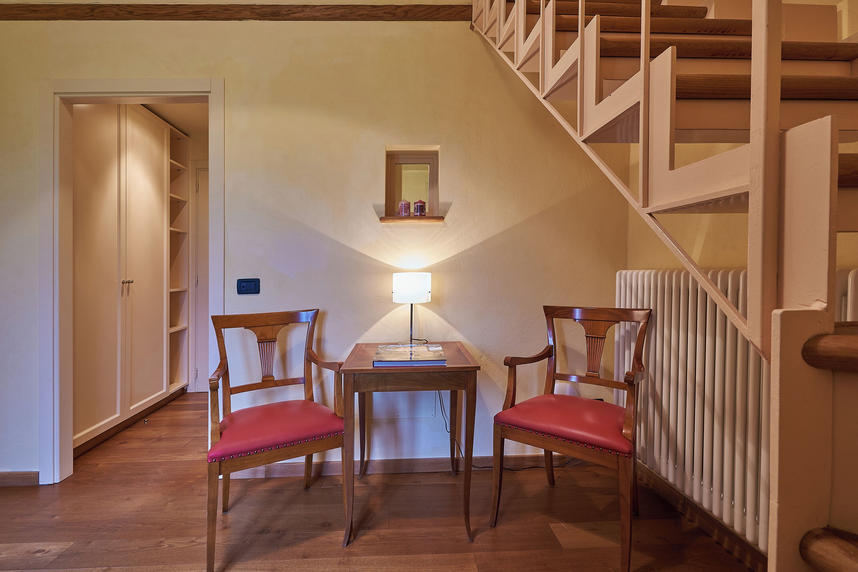 Una habitación con una mesa de madera, dos sillas, un ventanal pequeño y una escalera.
