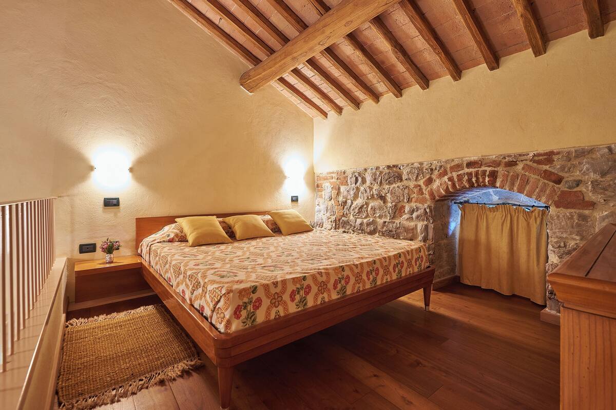 Une chambre avec un lit en bois, un mur en pierre et un plafond en bois.