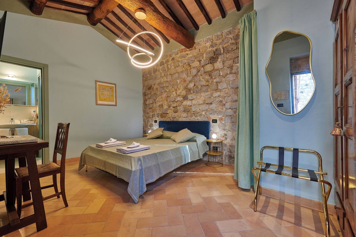 Une chambre avec un mur en pierre, un lit avec une tête de lit bleue, une chaise en bois, une petite table et un miroir.