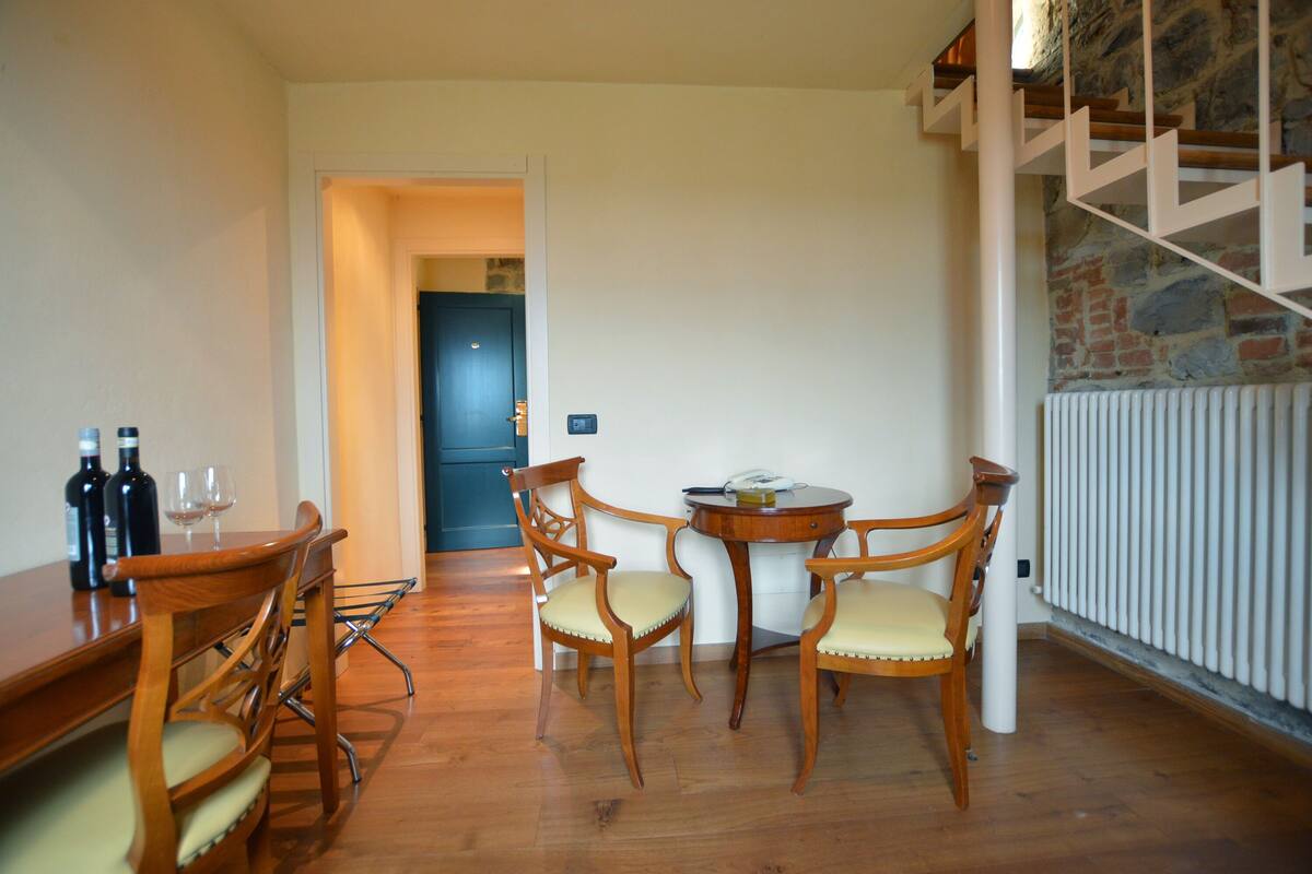 Un coin repas avec une table et des chaises en bois, une petite table ronde avec une bouteille et un verre, et un escalier avec un mur en pierre.