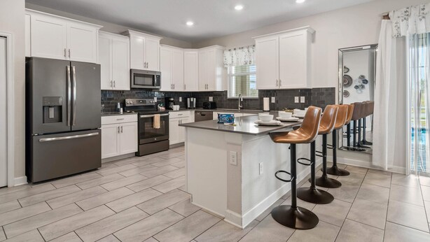 A modern kitchen with white cabinets, stainless steel appliances, and a central island with bar stools. - 8848 Cabot Cliffs Drive (Davenport)