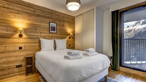 A bedroom with a wooden wall, a bed with white linens, two wall-mounted lamps, and a window with a mountain view.