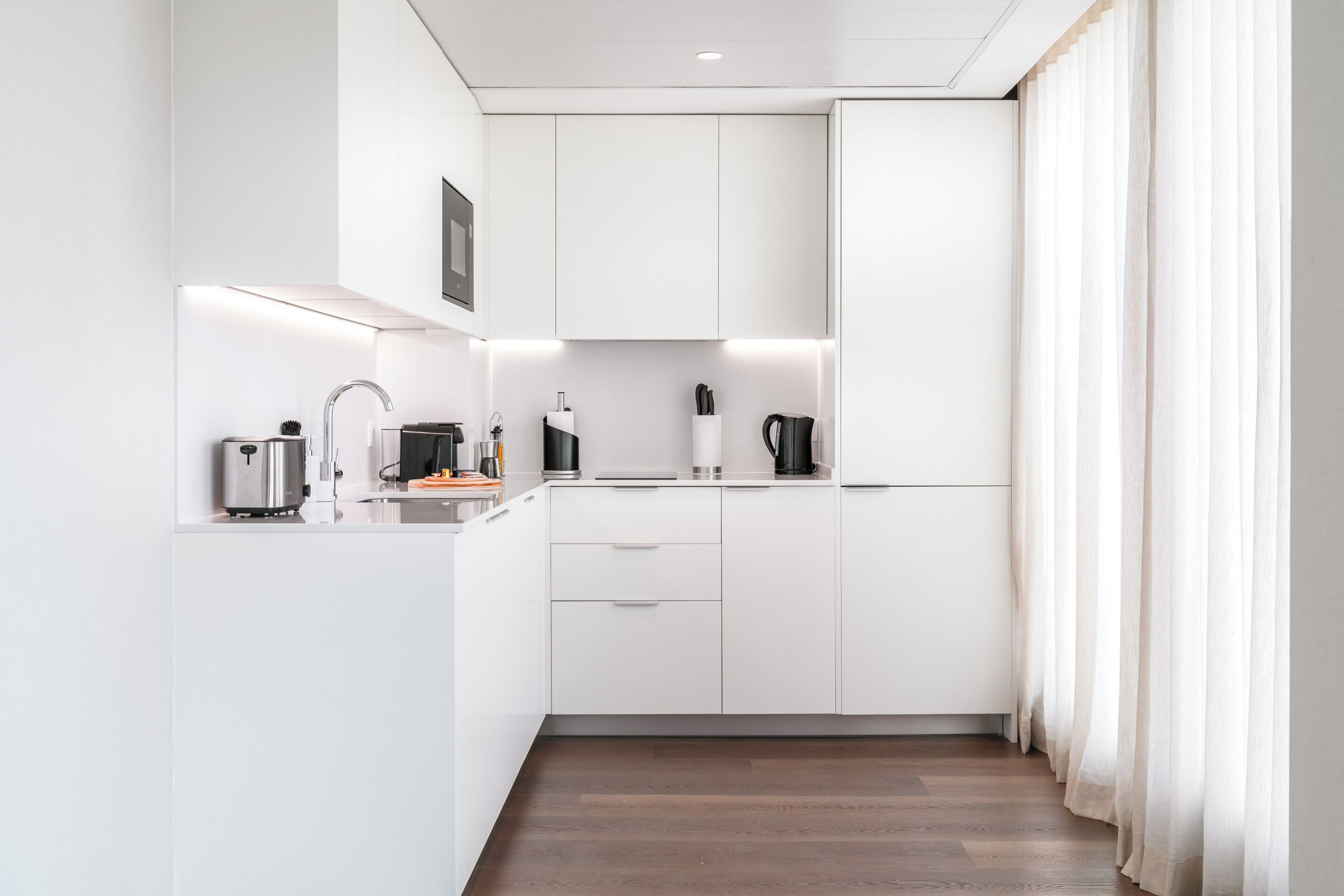 Una cocina moderna con armarios blancos, un hervidor de acero inoxidable, una cafetera y un tostador.