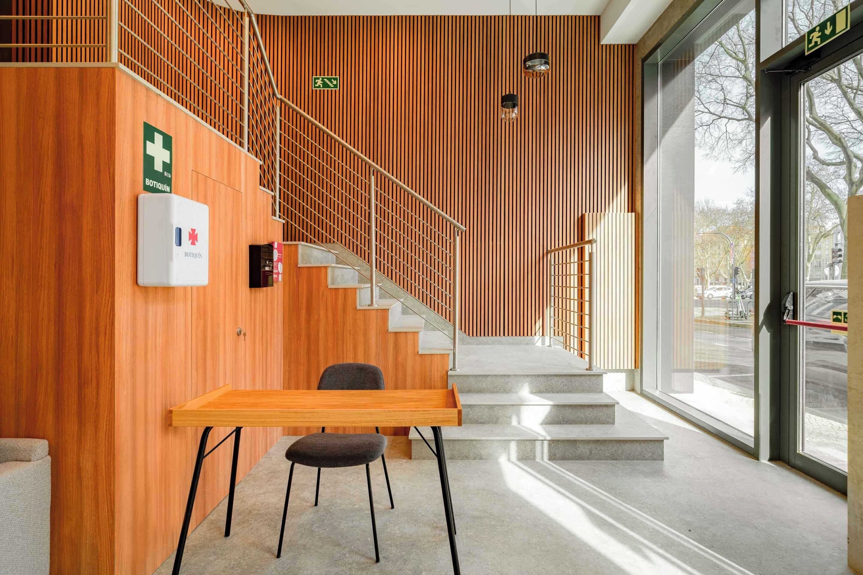 Un intérieur moderne avec un mur en bois, un escalier, une table avec des chaises et une fenêtre donnant sur l’extérieur.
