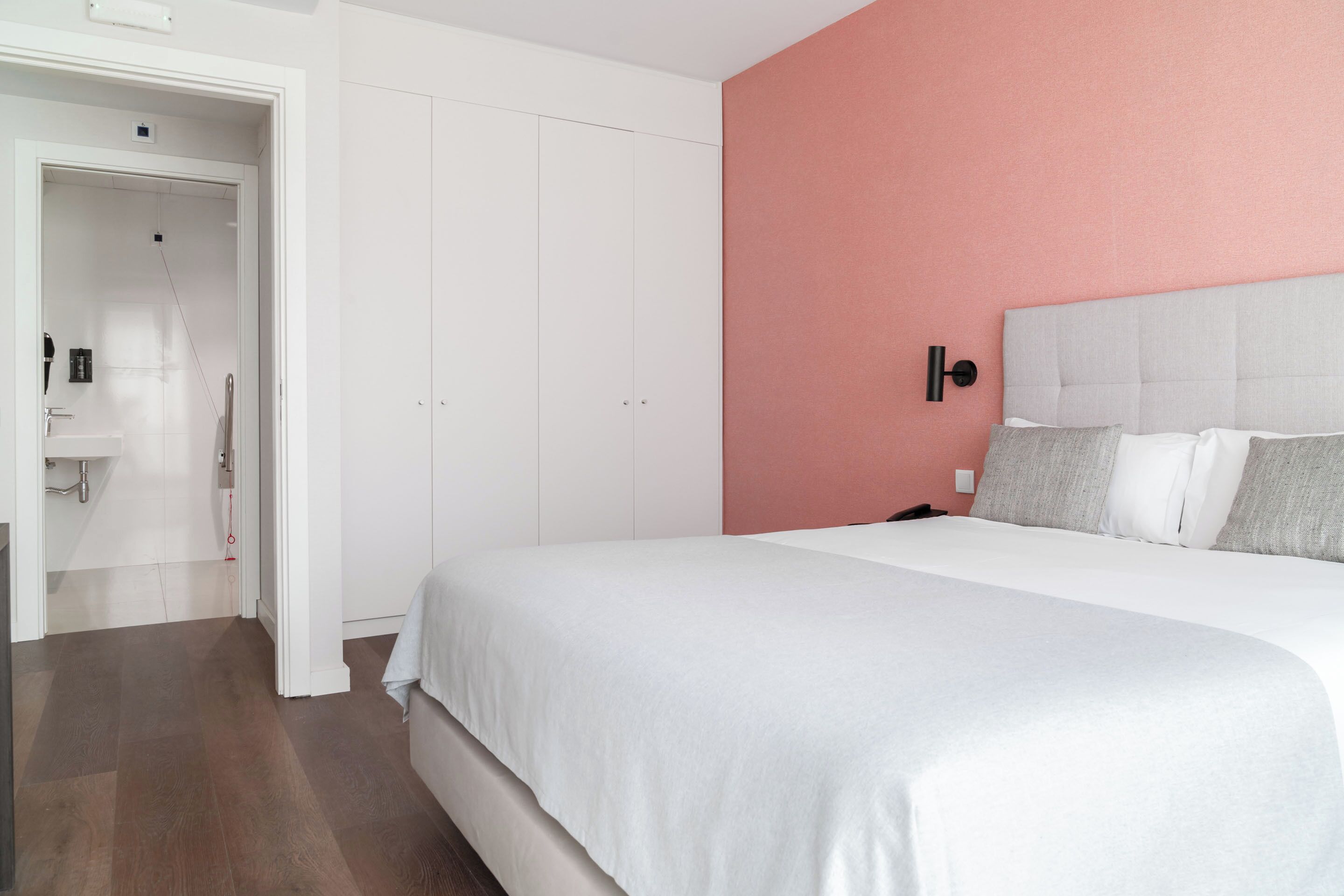 Ein Schlafzimmer mit Bett, Kleiderschrank und einem durchgehenden Türrahmen sichtbarem Badezimmer.