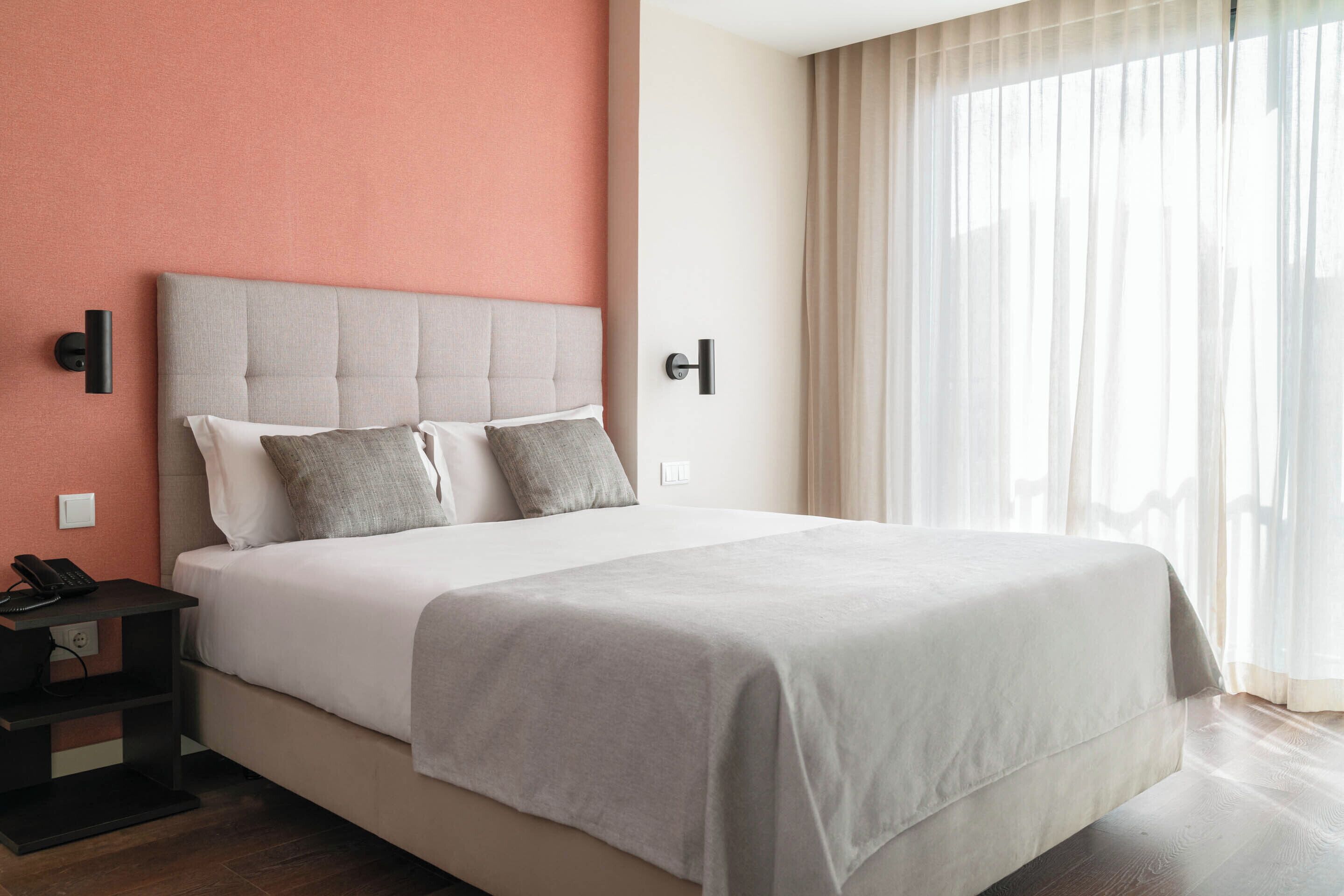 A hotel room with a bed, a nightstand, a telephone, and a window with curtains.