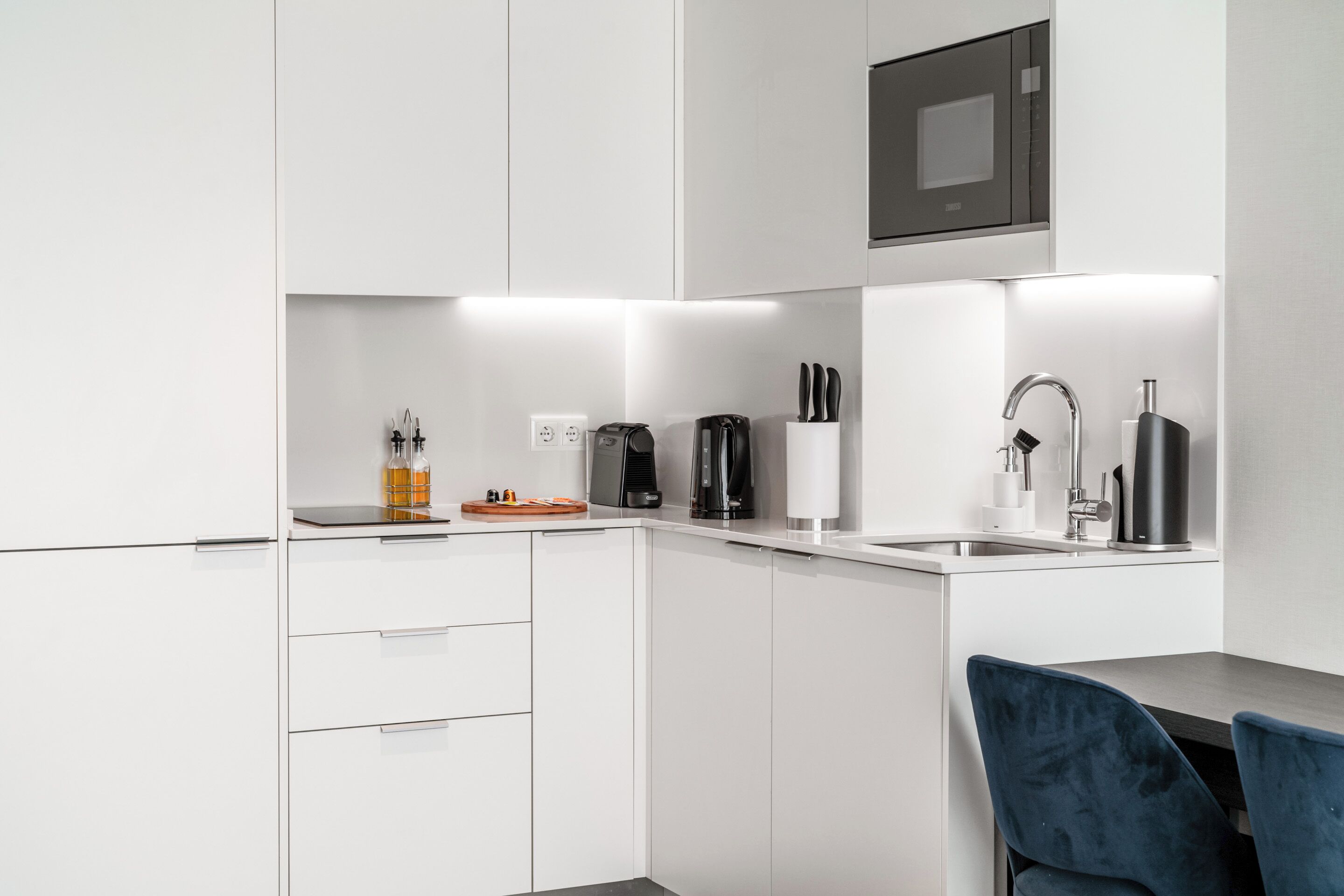 Una cocina moderna con armarios blancos, microondas integrado, cafetera y un lavamanos.