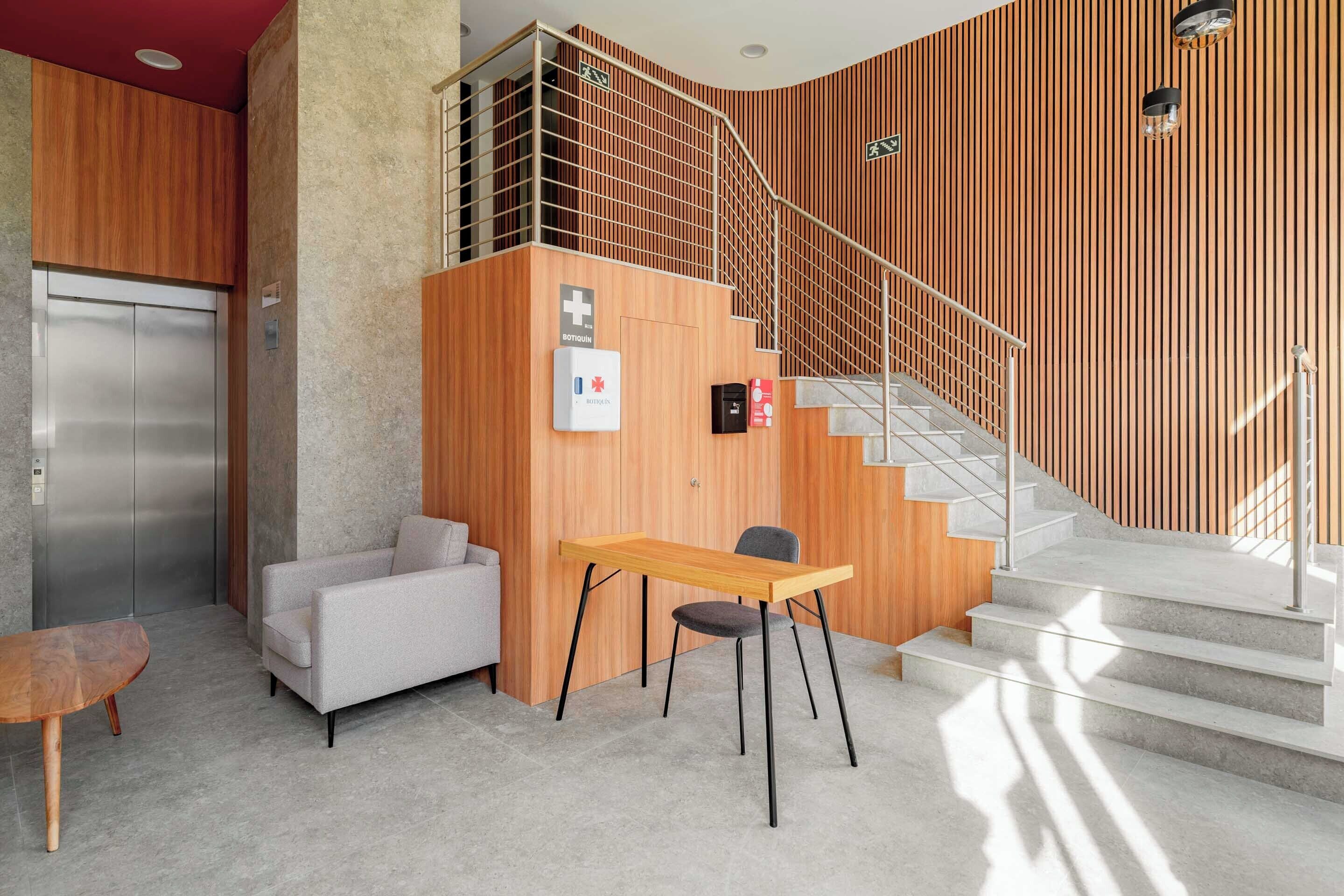 Un hall d’entrée moderne avec un comptoir d’accueil en bois, un canapé, une table et un escalier.
