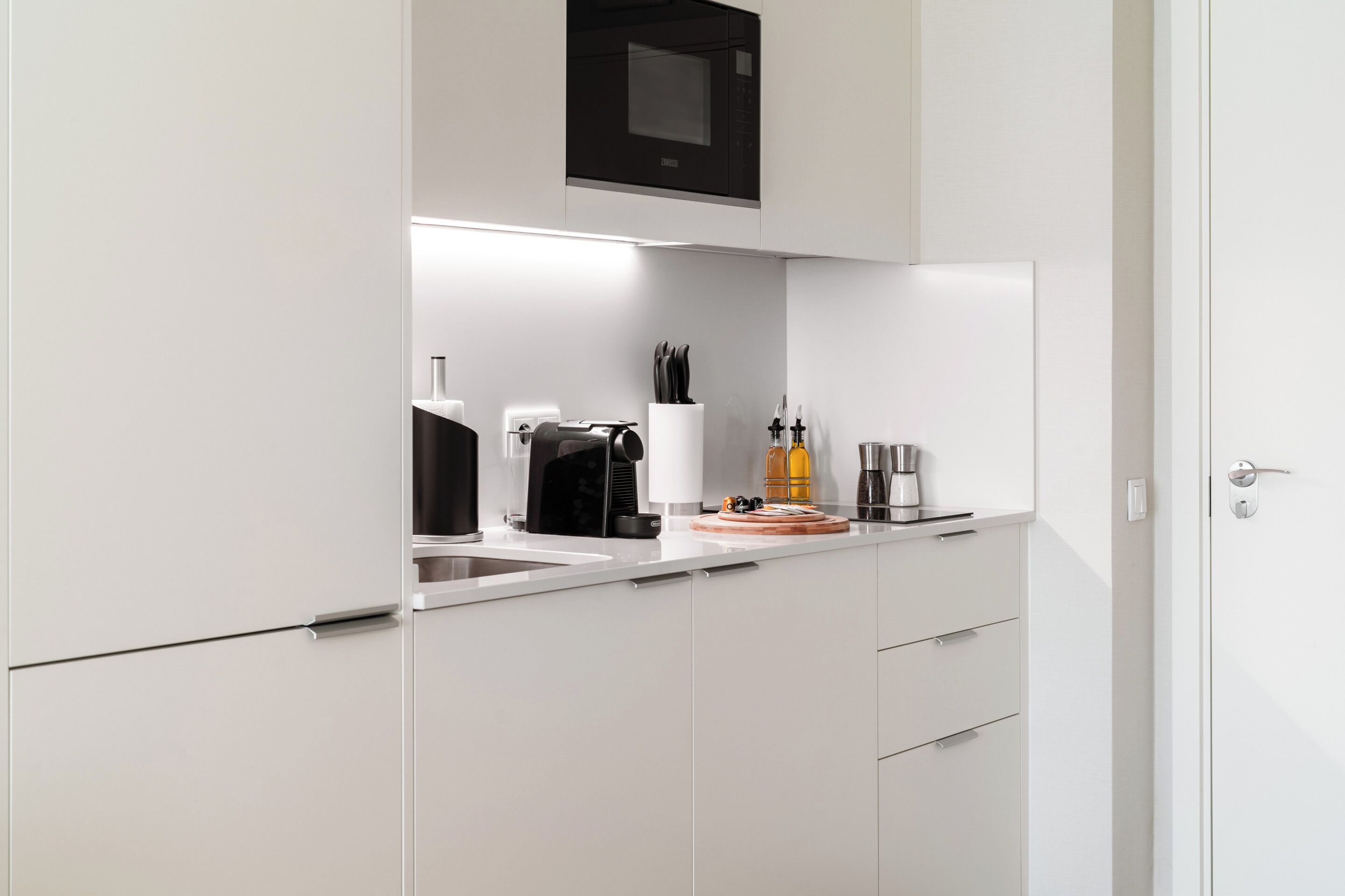 Una cocina moderna con armarios blancos, microondas, cafetera y bloque de cuchillos.