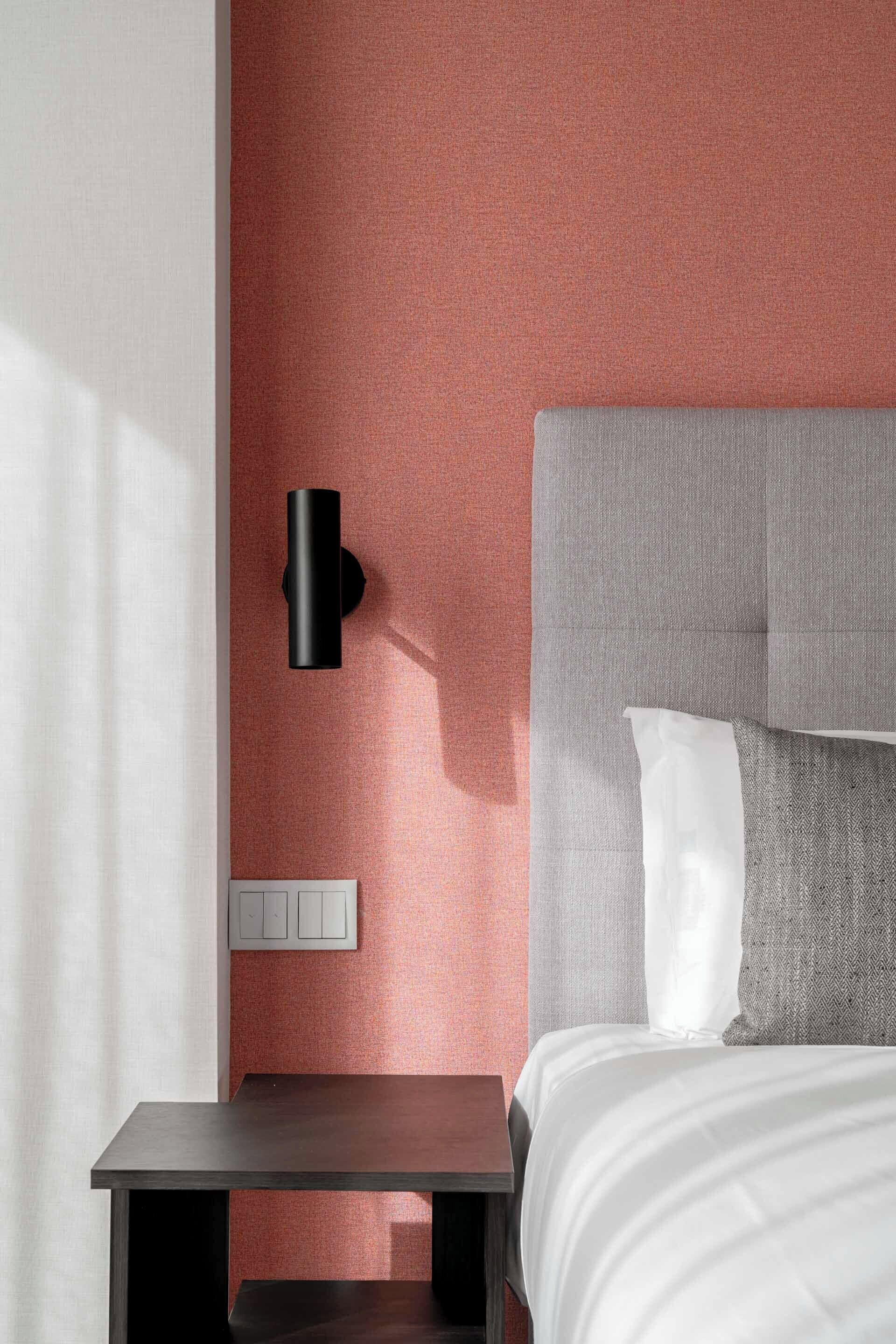 A modern bedroom with a grey upholstered headboard, a white pillow, a bedside table, and a wall-mounted light fixture.