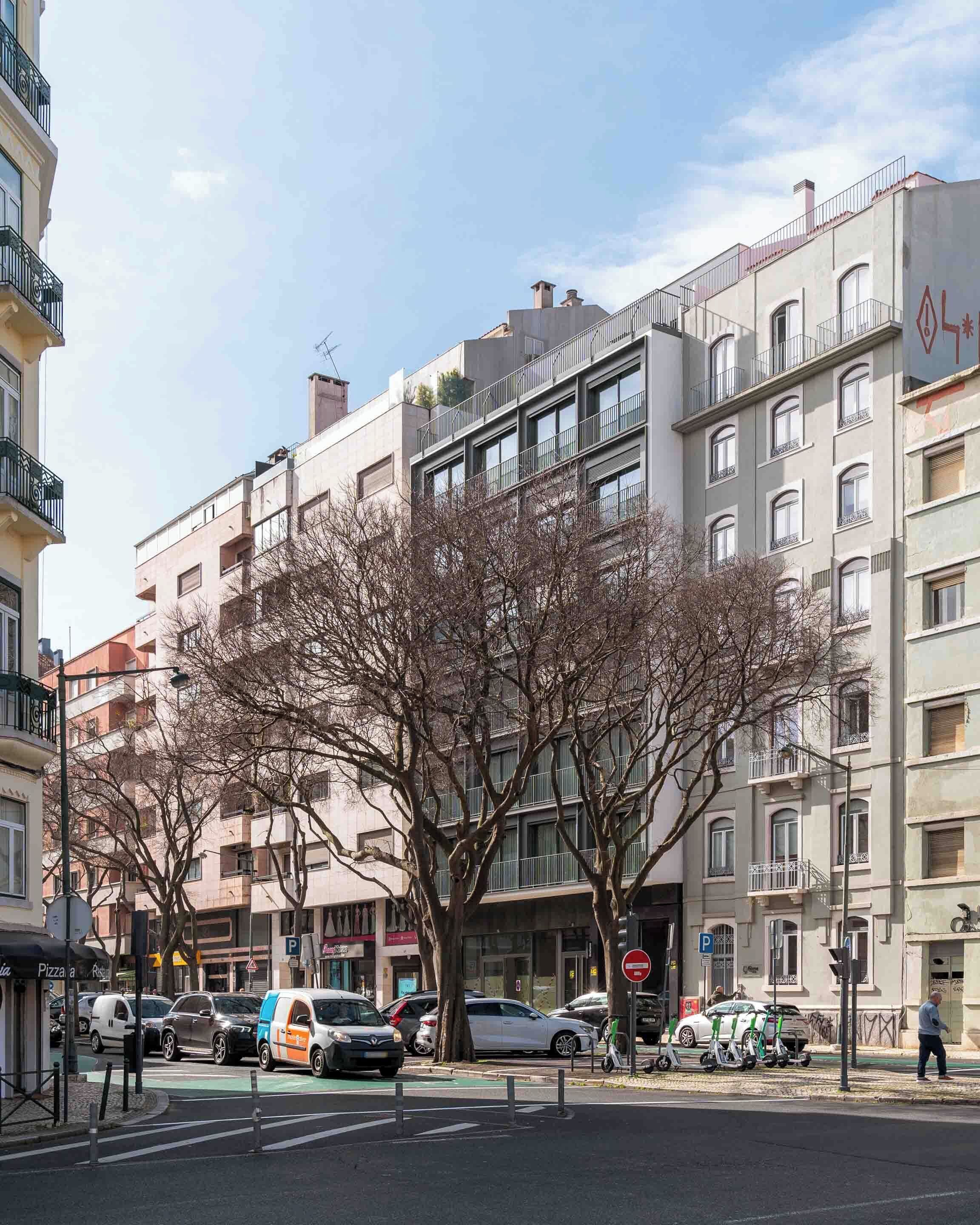 Un immeuble à plusieurs étages doté de balcons, avec des voitures garées et une rue bordée d’arbres.