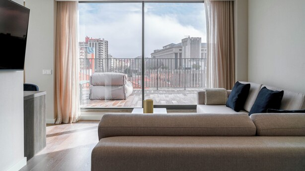 A modern living room with a large window, a sofa, a TV, and a balcony with a view of the city. -  Limehome Lisbon Campo Pequeno (Lisbon)