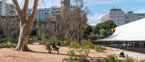 A park with a large tree, a covered pavilion, and buildings in the background.