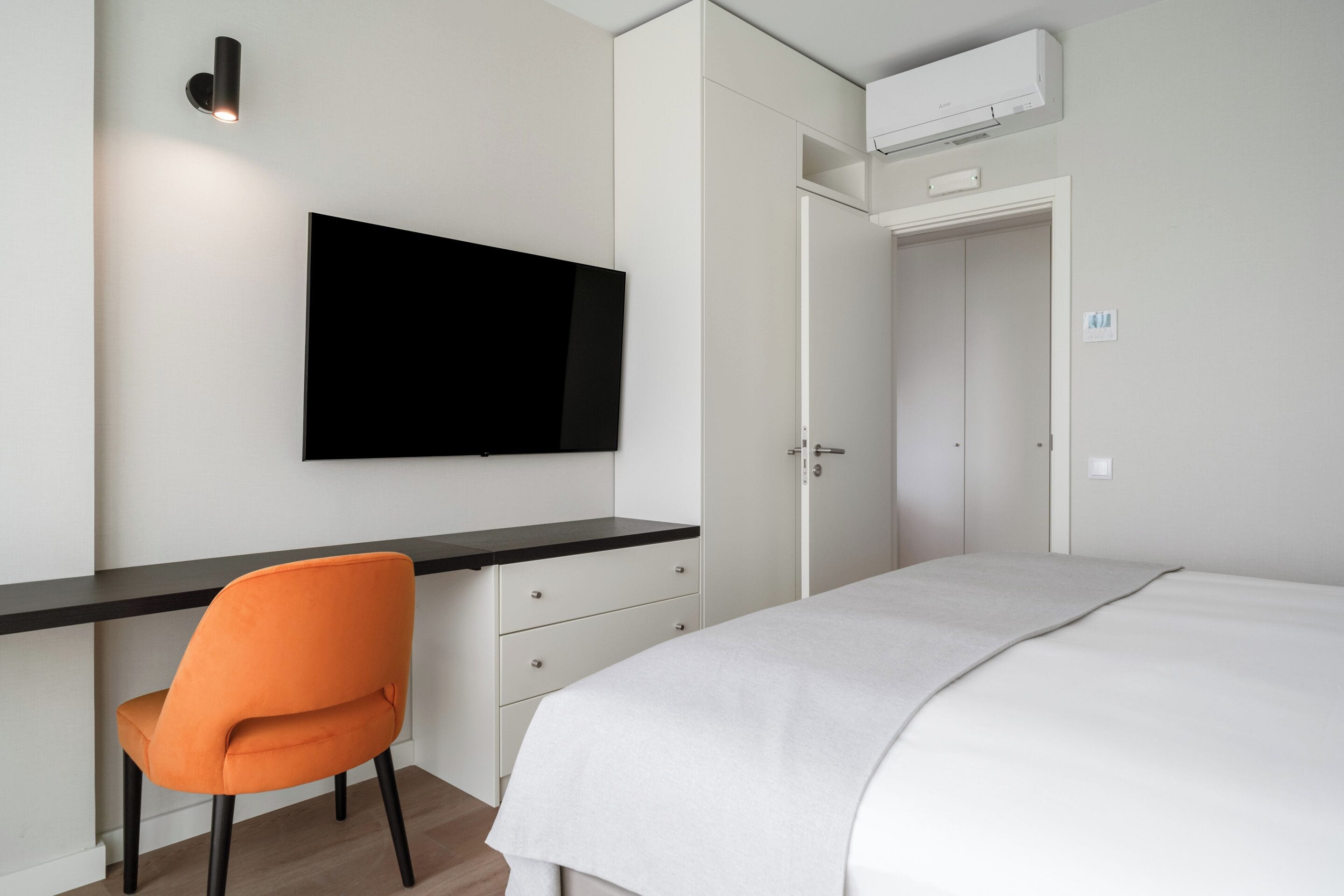 Un dormitorio con una cama, un escritorio con una silla, un televisor y un equipo de aire acondicionado.