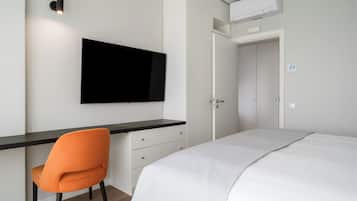Un dormitorio con una cama, un escritorio con una silla, un televisor y un equipo de aire acondicionado.