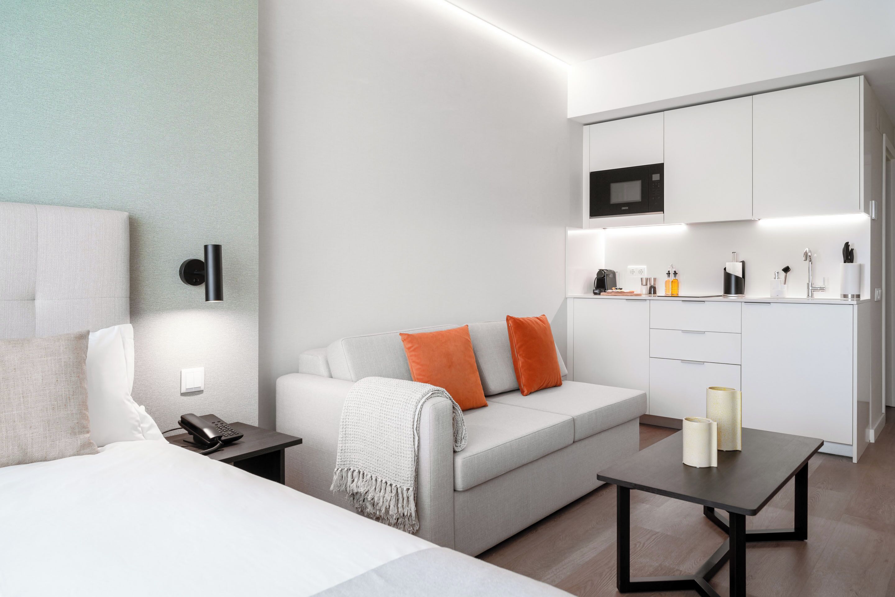 Ein modernes Hotelzimmer mit Bett, einer Couch, einem kleinen Tisch und einer Küchenzeile.