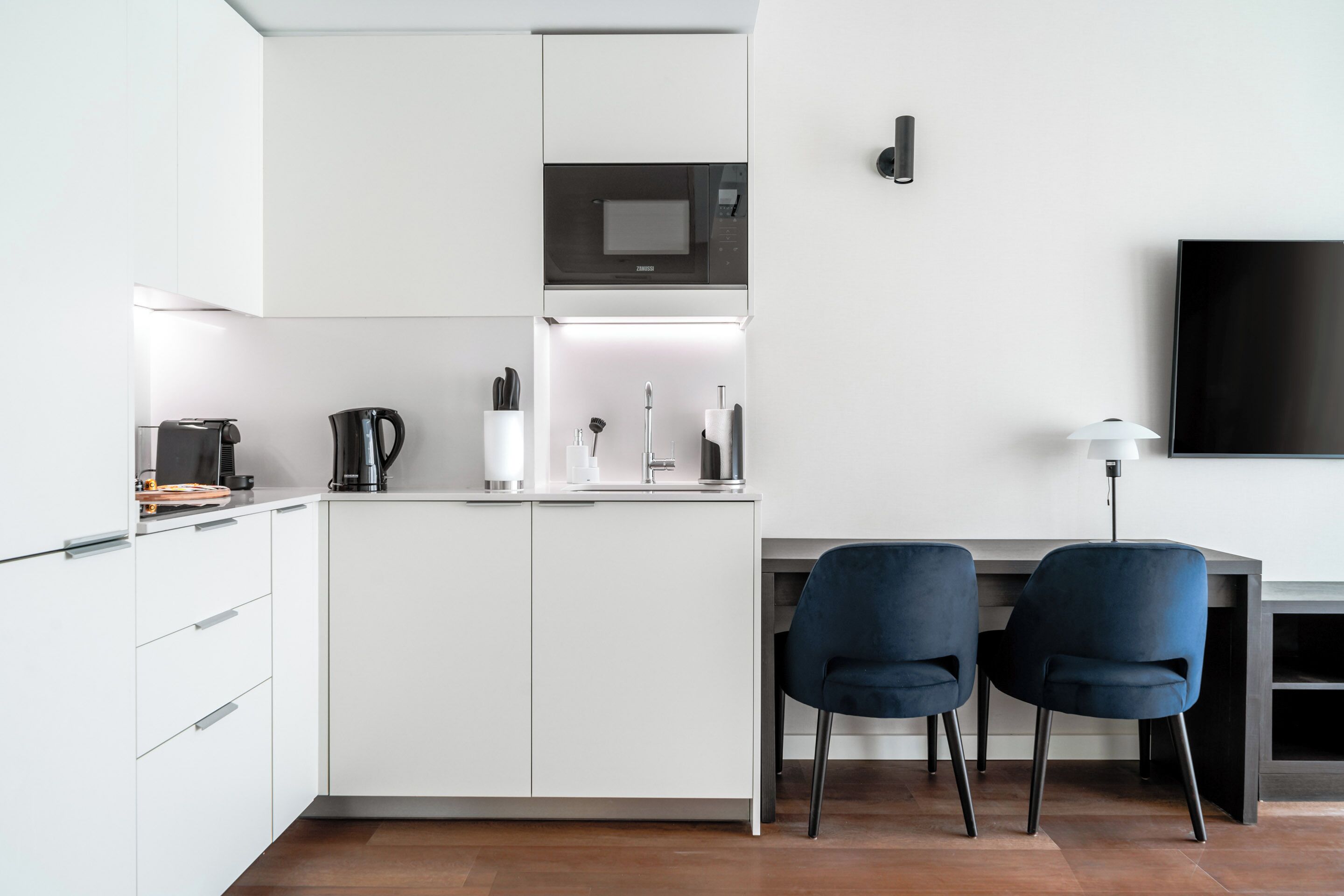 A modern kitchen with white cabinets, a microwave, a coffee maker, and two blue chairs.