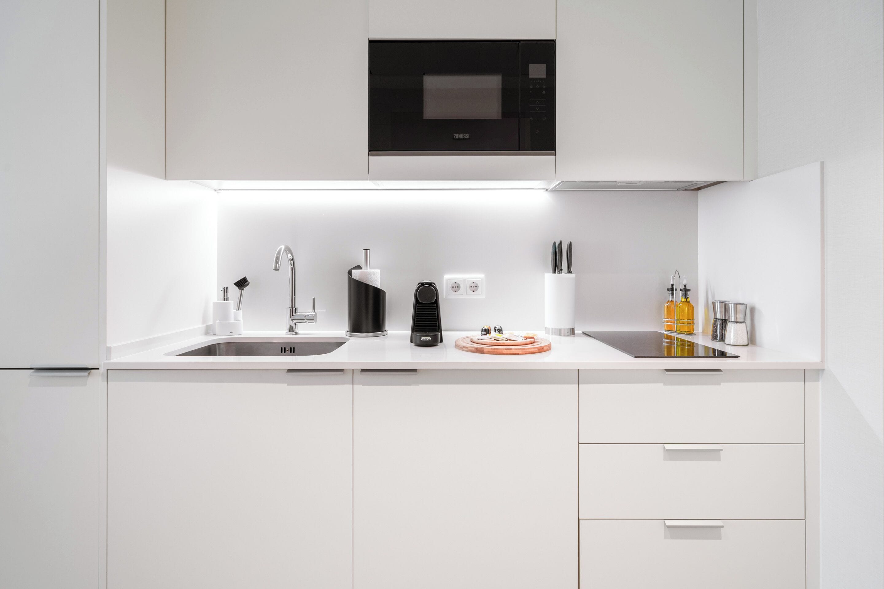 Une cuisine moderne avec des meubles blancs, un micro-ondes noir, une machine à café et un évier.