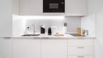 Une cuisine moderne avec des meubles blancs, un micro-ondes noir, une machine à café et un évier.