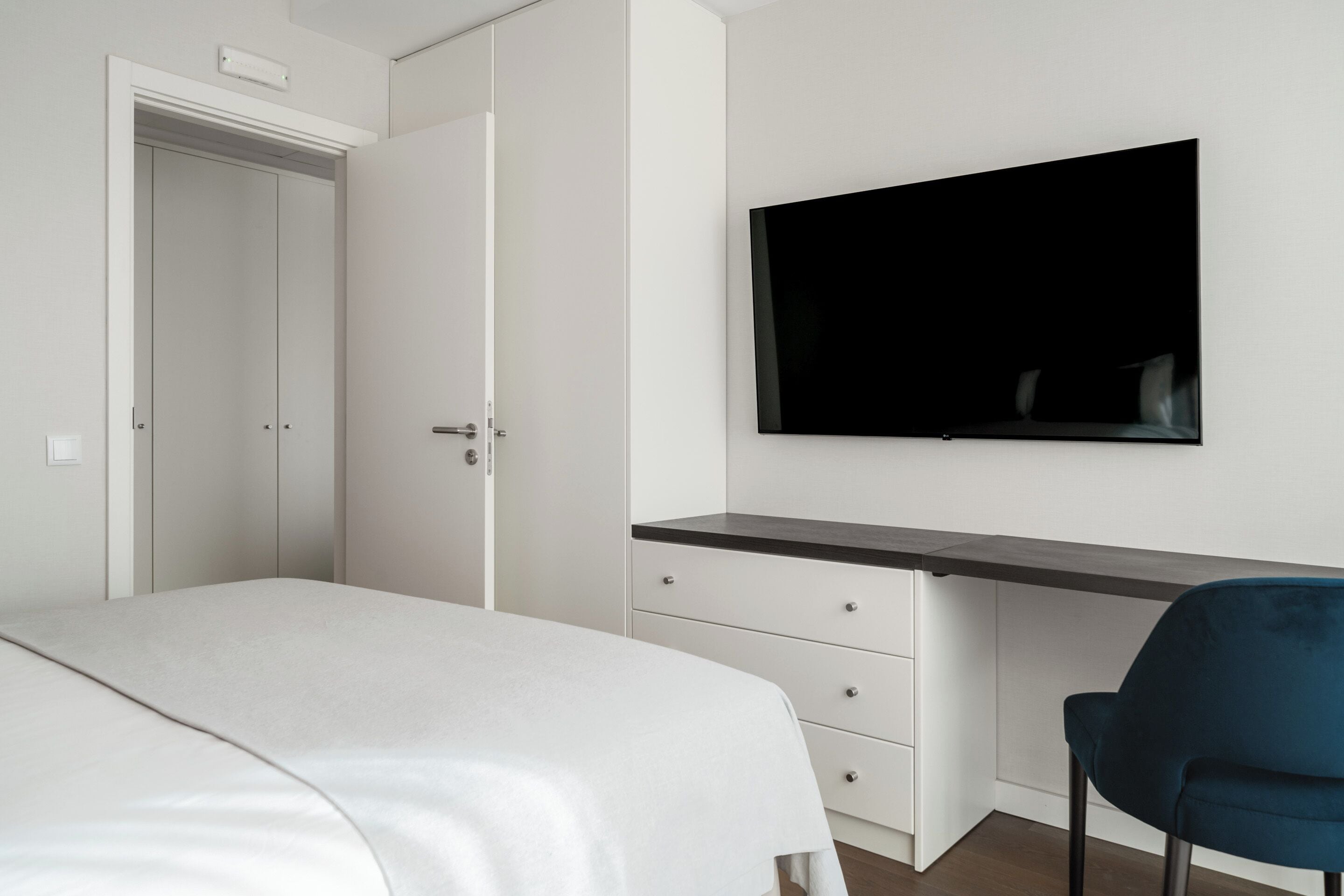 Une chambre à coucher comprenant un lit, un bureau, une chaise et un téléviseur fixé au mur.