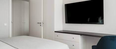 Une chambre à coucher comprenant un lit, un bureau, une chaise et un téléviseur fixé au mur.