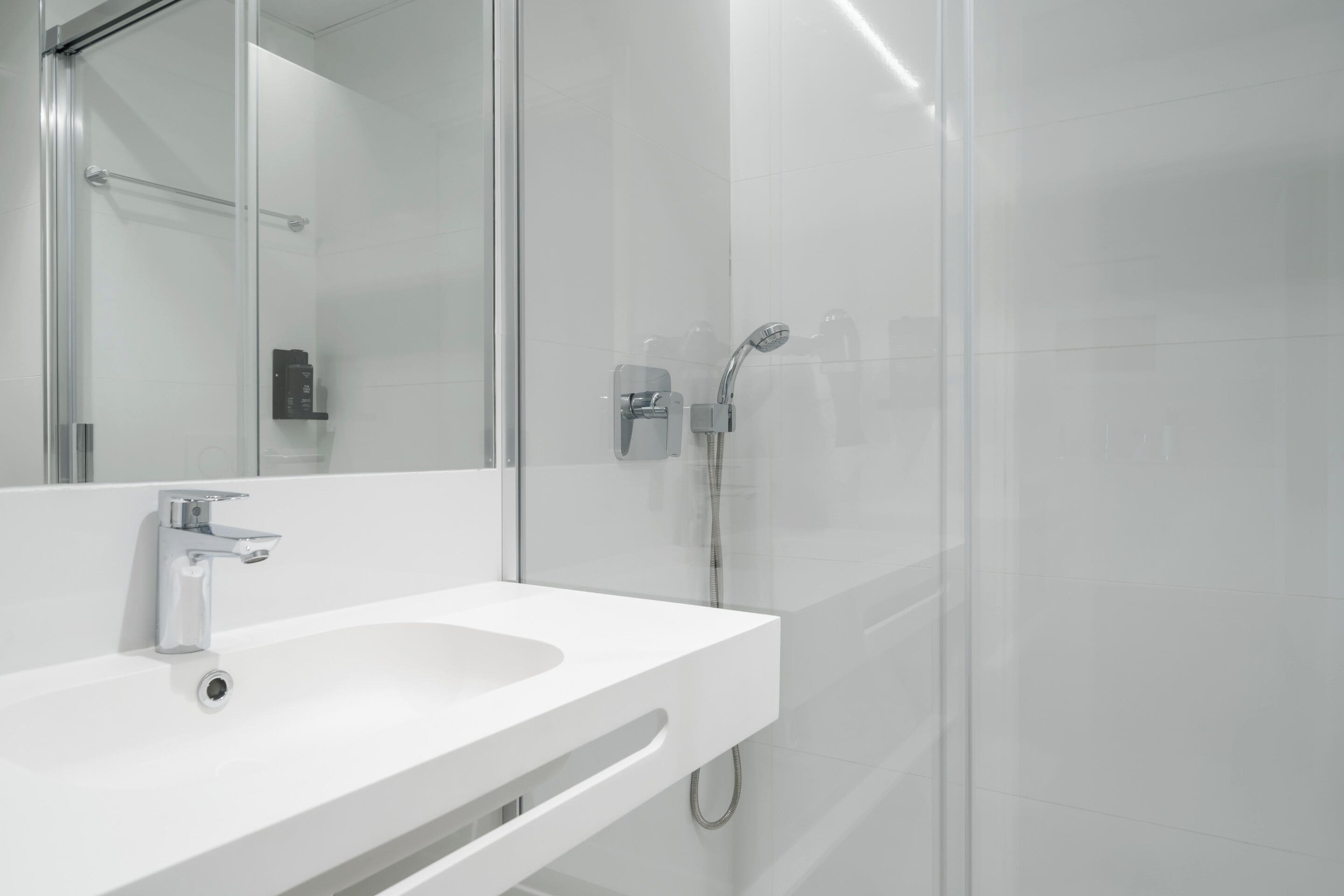 A modern bathroom with a white sink, a mirror, and a glass-enclosed shower area.
