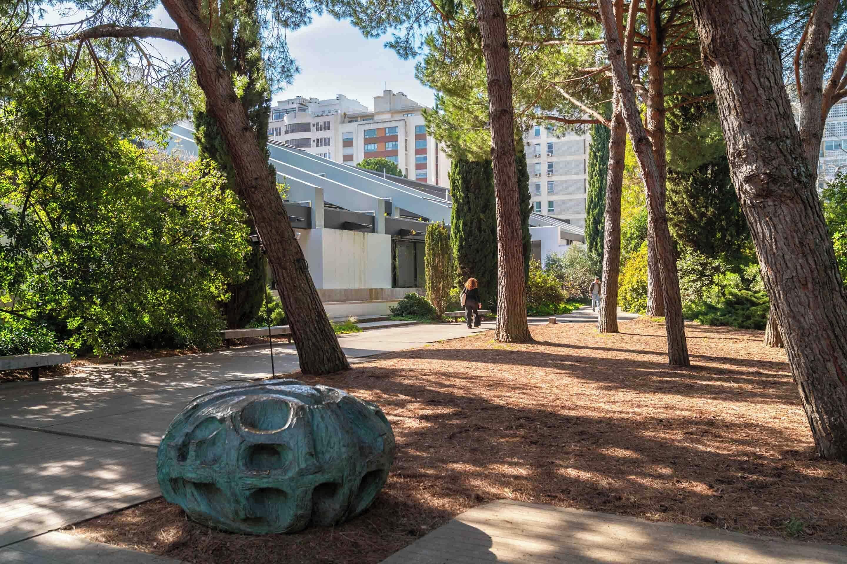 Un parque con árboles, una escultura y un edificio al fondo.