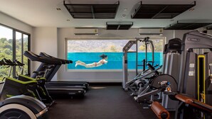 A gym with exercise equipment, a large window with a view of a swimming pool, and air conditioning units on the ceiling.