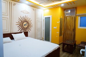 A bedroom with a bed, a small table, a chair, a mirror, and a window. - KAUSHIKI GARDEN (Patna)