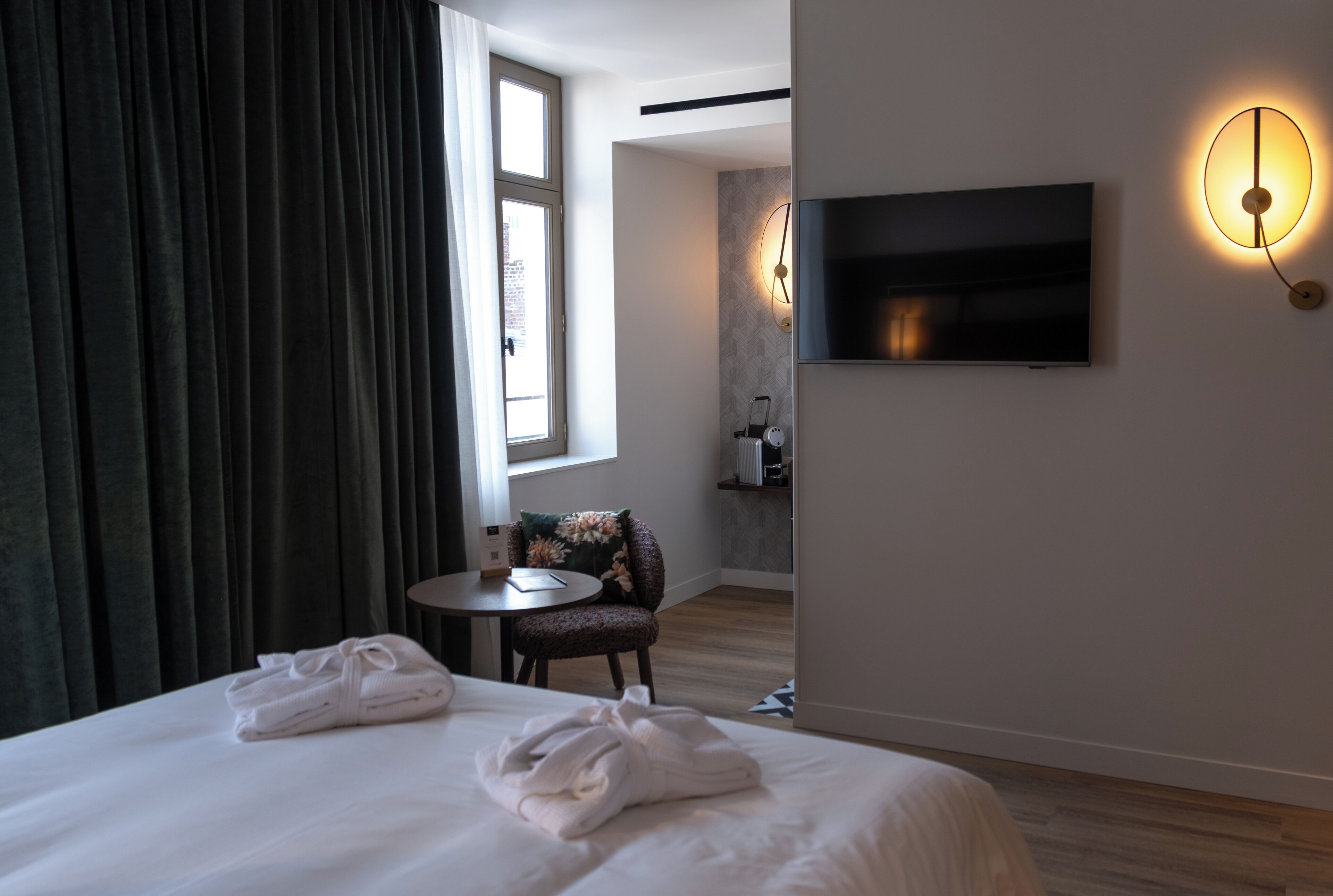 A hotel room with a bed, a TV mounted on the wall, a small table, and a chair.