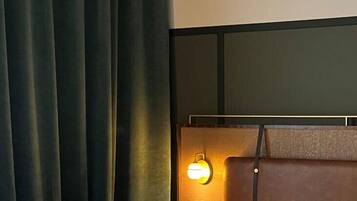 Quarto com cama, cabeceira com luz e cortina.