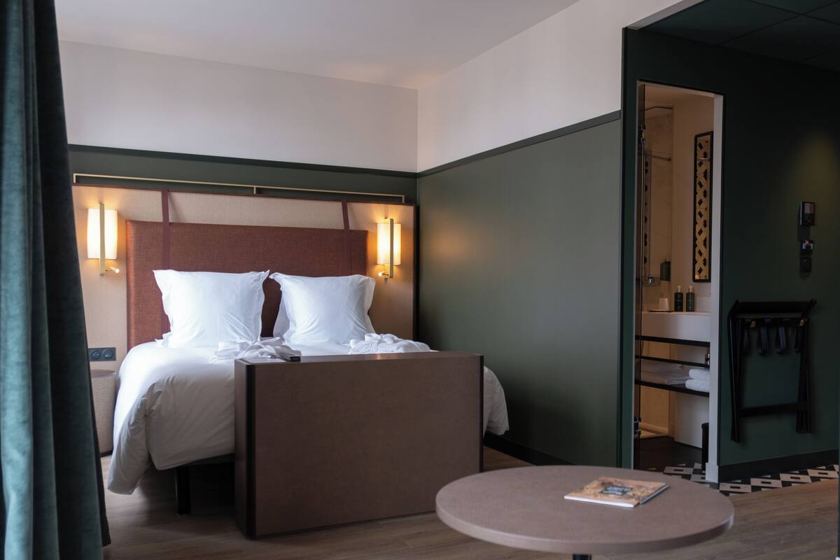 A hotel room with a bed, bedside table, and a round table with a book.